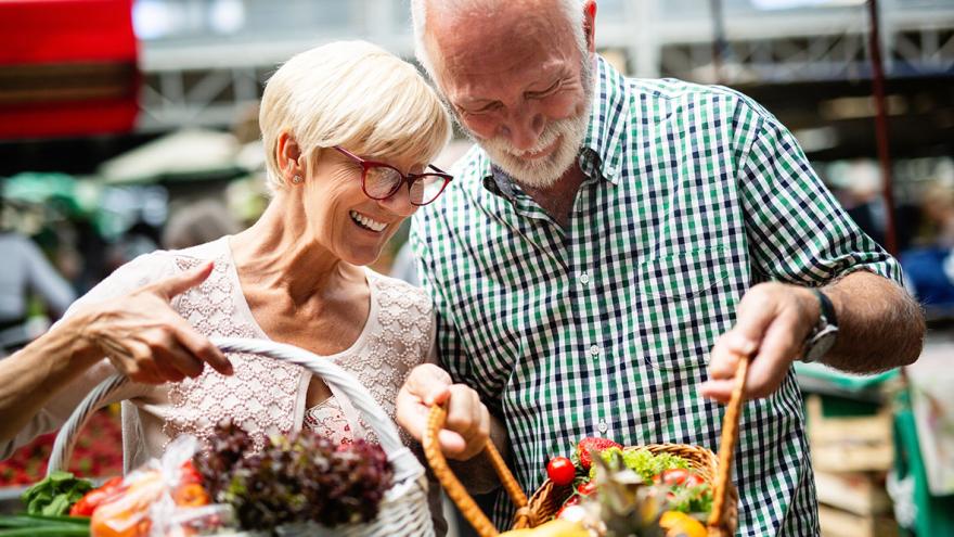 Essen mit Genuss, auch im Alter: Ein älteres Paar kauft zeigt sich gegenseitig die Einkäufe auf dem Markt