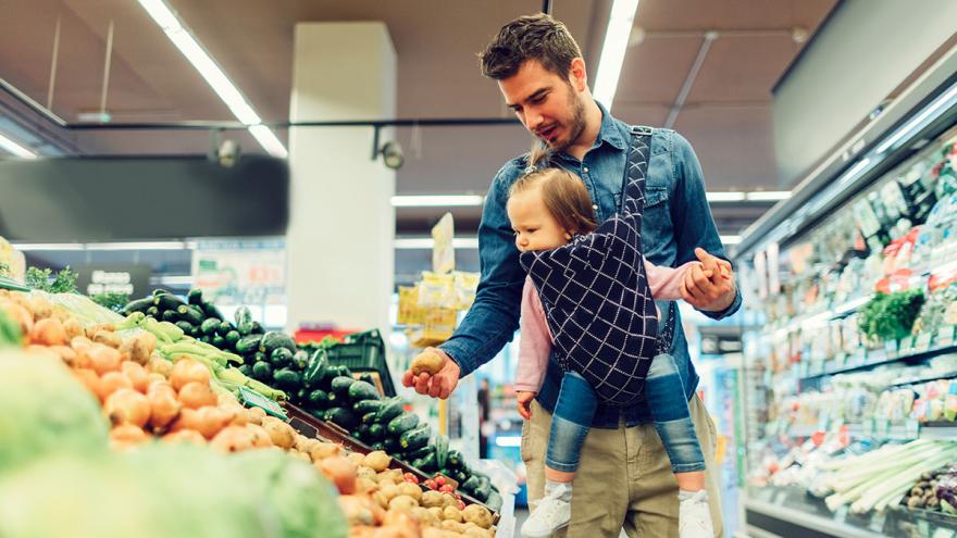 Nachhaltig einkaufen: Ein Mann mit Baby in der Trage steht am Gemüseregal 