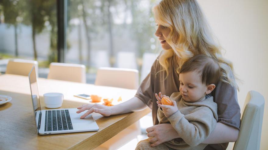 Altersvorsorge für Frauen und junge Familien: Eine junge Frau hat ein Kind auf dem Schoß und sitzt am Tisch vor einem Laptop 