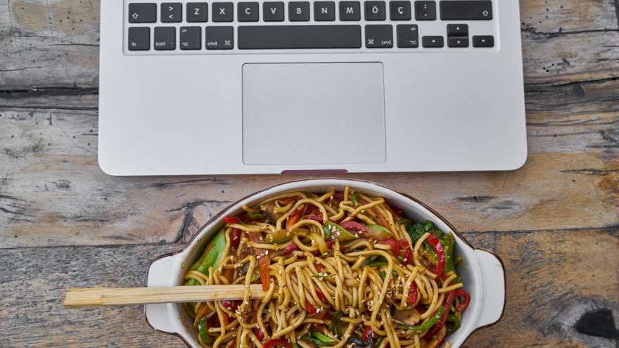 Ein asiatisches Nudelgericht mit Gemüse vor einem Laptop