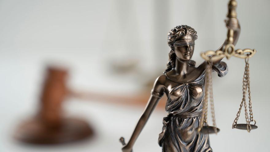 Skulptur der Justizia, im Hintergrund ein Hammer als Symbol des Gerichtsurteils
