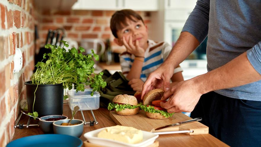 Ein Mann bereitet für einen Jungen ein gesundes belegtes Brötchen zu 