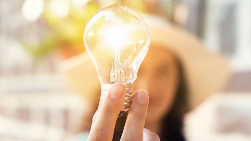 Eine Frau, unscharf in Hintergrund, hält eine leuchtende Glühlampe hoch  