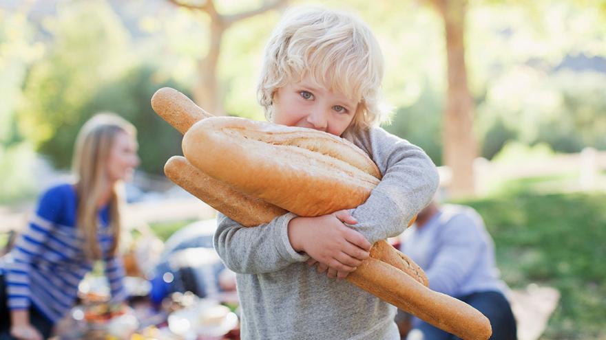 Ein kleiner Junge trägt mehrere Brote auf dem Arm 
