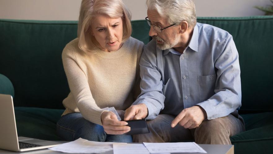 älteres Paar schaut besorgt auf Handy, Rechnungen im Vordergrund