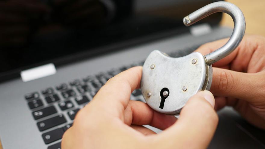 Jemand hält ein offenes Vorhängeschloss in der Hand, im Hintergrund ein Laptop