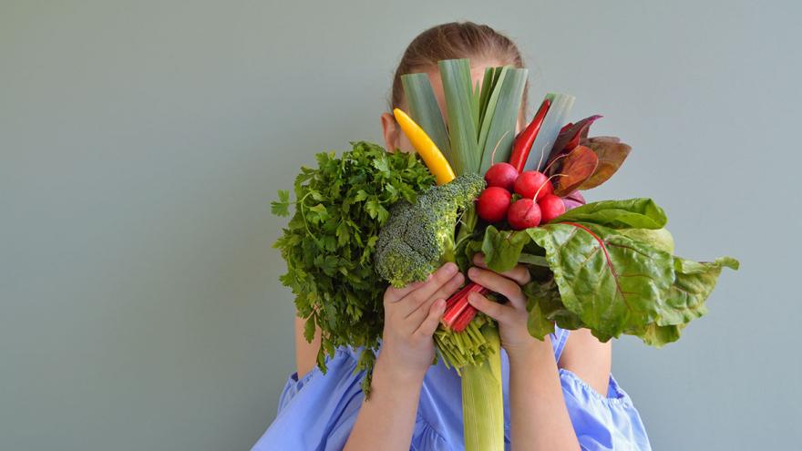 Eine Frau hält einen Strauß aus Gemüse vor ihr Gesicht 