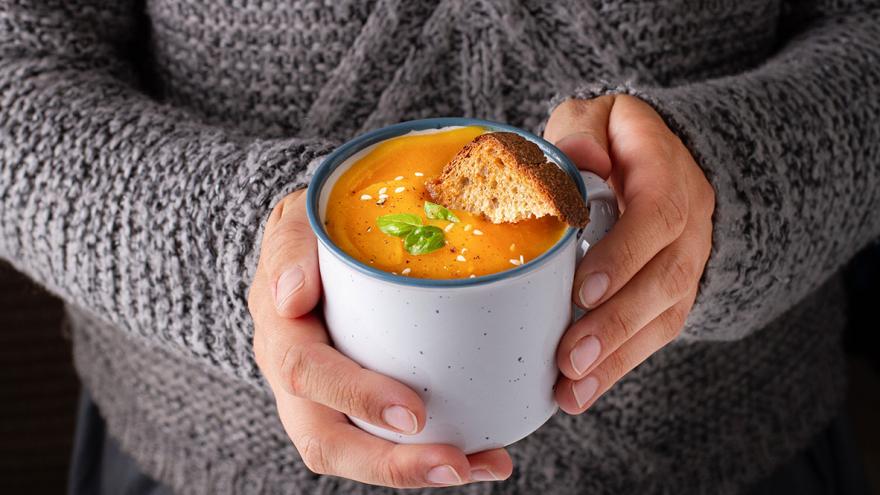 Jemand hält eine Tasse mit Suppe in den Händen