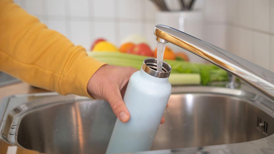 Jemand füllt am Wasserhahn seine Trinkflasche auf