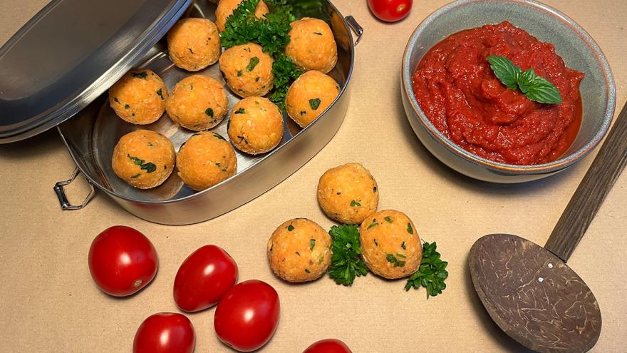 Linsen-Couscous-Bällchen in einer Lunchbox, eine Schale mit selbstgemachtem Ketchup, Deko aus Tomaten 
