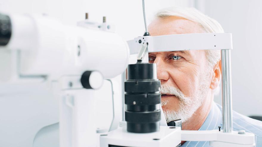Ein älterer Mann sitzt in einer Arztpraxis vor einem Gerät zur Untersuchung der Augen 