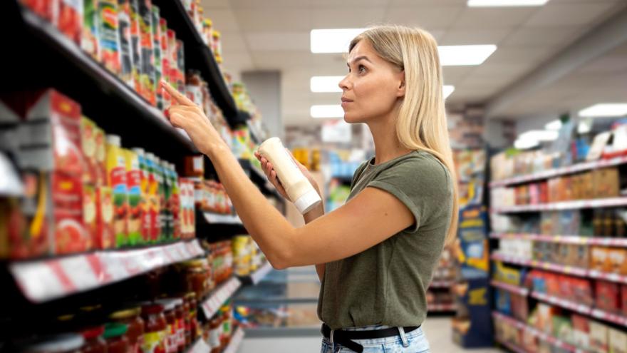 Eine Frau steht mit kritischem Blick am Supermarktregal und vergleicht die Preise 