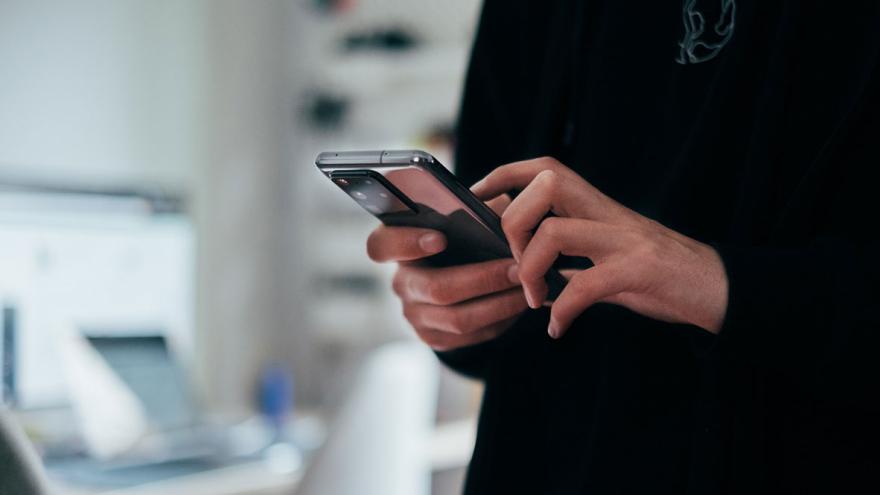 Eine Person mit dunklem Pullover hält ein Smartphone in der Hand