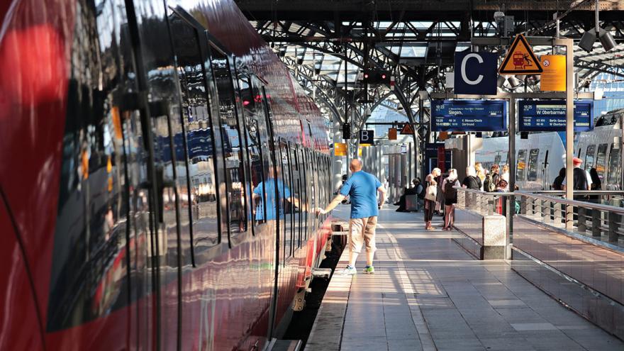 Ein ZUg steht auf einem Gleis im Bahnhof, ein einzelner Passagier versucht einzusteigen