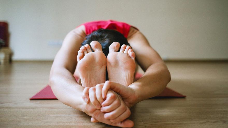 Eine Frau sitzt auf einer Yogamatte in Vorbeuge und umfasst ihre Füße 