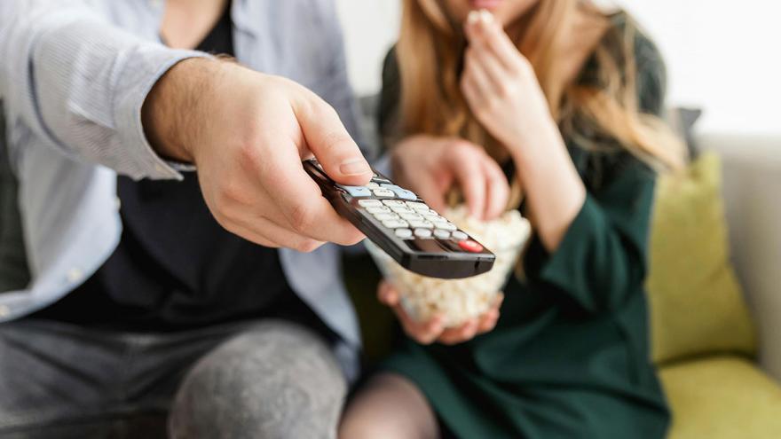 Zwei paar Hände halten eine Fernbedienung und eine Schüssel mit Popcorn  