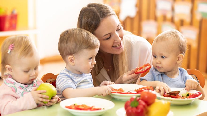 Eine Frau sitzt mit drei Kleinkindern beim Essen am Tisch