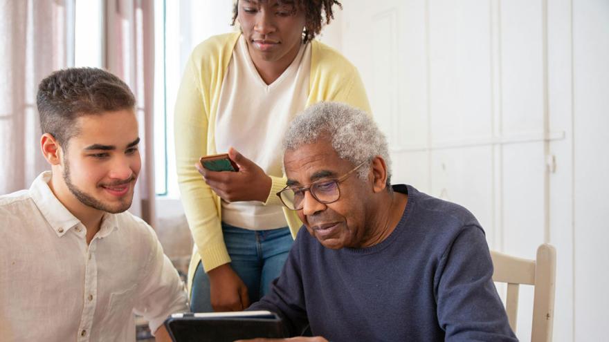 Ein älterer Mann mit einem Tablet-PC und ein jüngeres Paar beraten sich 