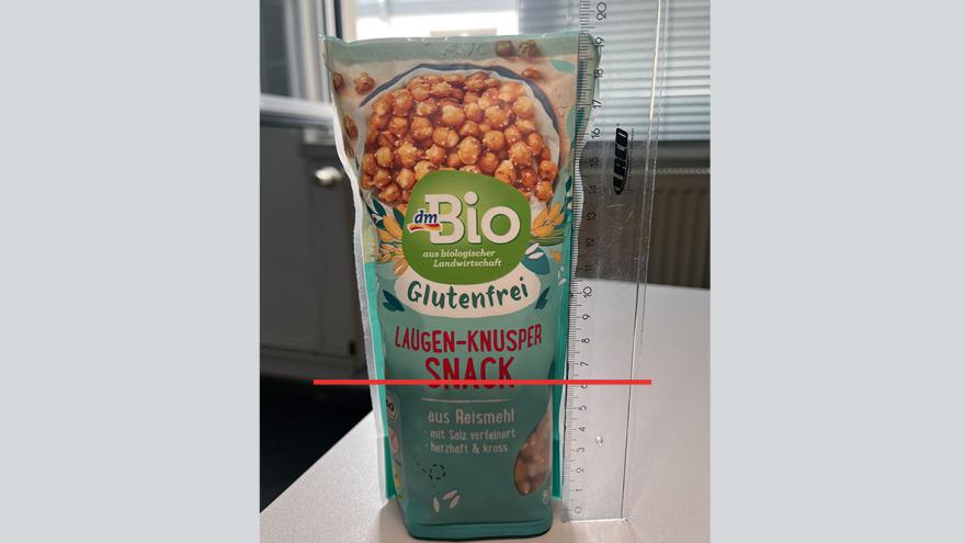 Foto der Verpackung des Laugen-Knusper Snack mit Lineal daneben. Im Gegenlicht lässt sich erkennen, dass die Verpackung nur zu einem Drittel gefüllt ist. 