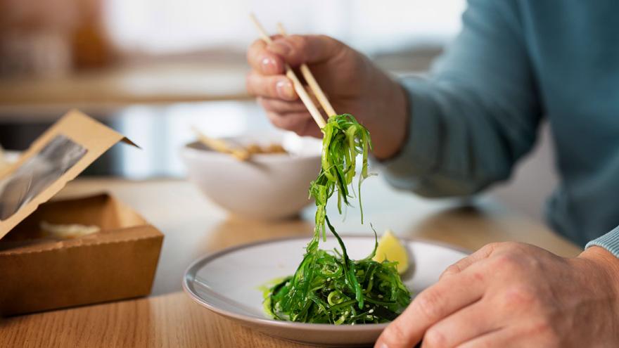Jemand isst mit Stäbchen einen Salat aus Algen