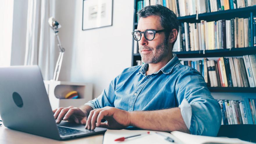 Ein Mann sitzt nachdenklich am Schreibtisch vor einem Laptop, ein Notizbuch daneben