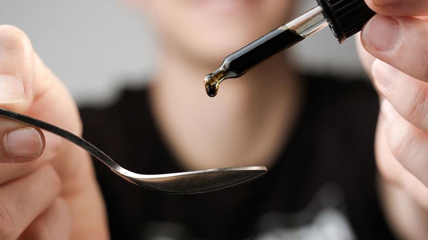 Jemand träufelt aus einer Pipette eine dunkle Flüssigkeit auf einen Löffel