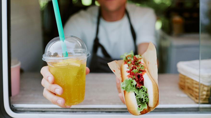 Jemand reicht einen Hotdog und einen Softdrink aus einer Imbisswagen nach draußen 