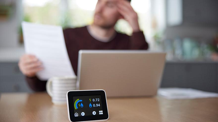 Ein Mann sitzt am Schreibtisch und liest Unterlagen, auf dem Schreibtisch ein smarter Energie-Verbrauchszähler