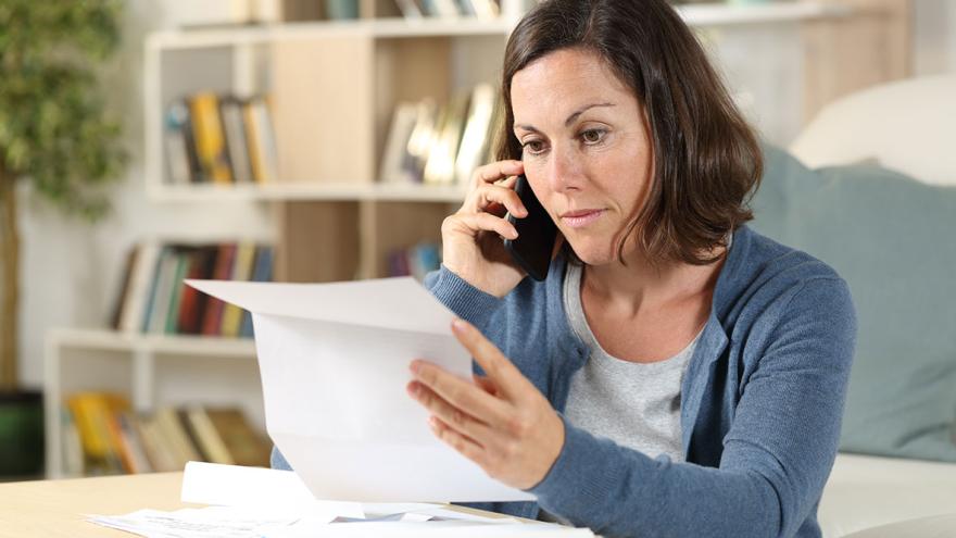 Eine Frau sitzt mit einem Brief in der Hand im Tisch und telefoniert  