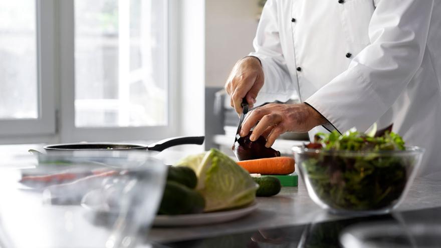 Eine Person in der Berufskleidung eines Kochs schneidet Gemüse schneidet 