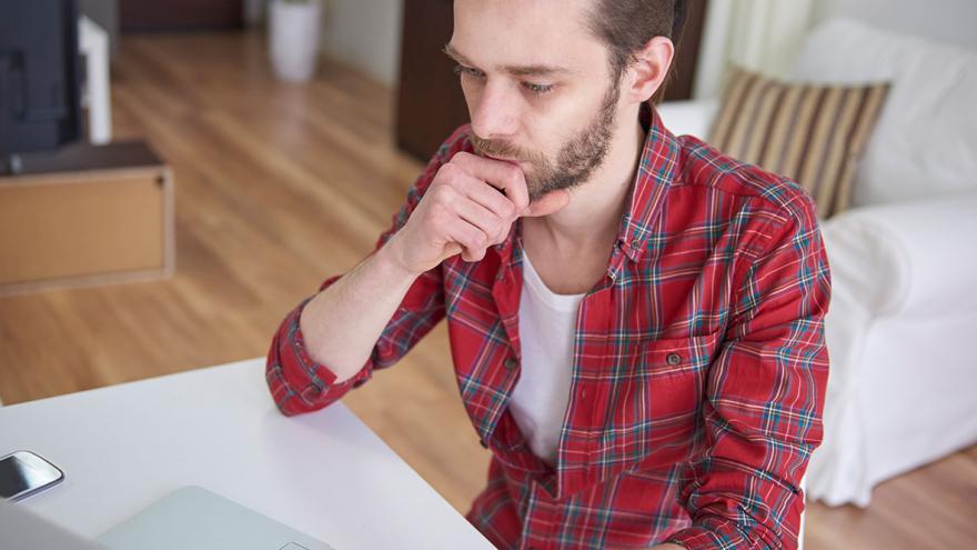 Ein Mann sitzt betroffen am Schreibtisch vor seinem Laptop 