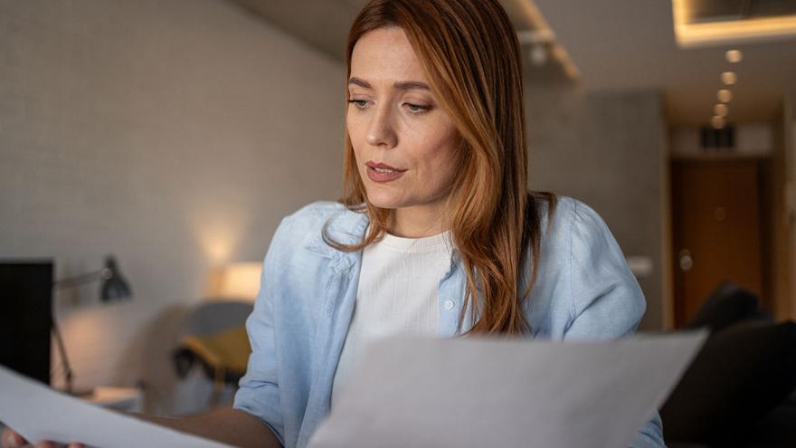 Eine Frau sitzt am Tisch und blickt verärgert auf einen Brief 