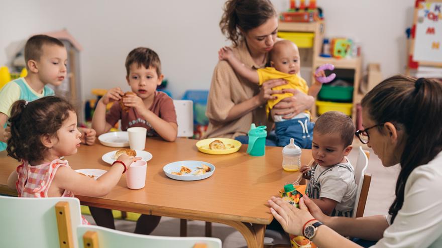 Kinder unterschiedlichen Alters sitzen mit zwei Betreuerinnen am Esstisch   