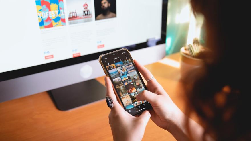 Eine Frau sitzt vor dem PC und blickt auf die Fotogalerie ihres Smartphones