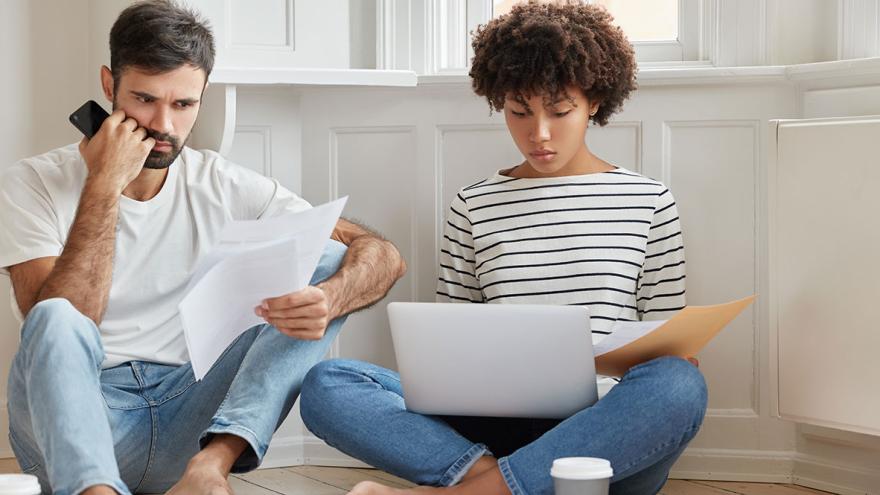 Ein Paar sitzt mit Telefon und Laptop in einer Wohnung auf dem Boden