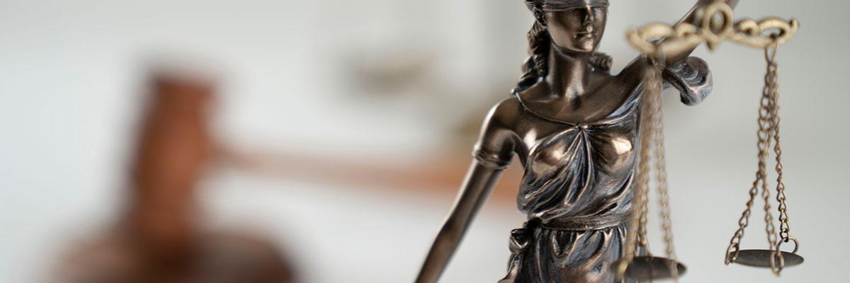 Eine Skulptur der Justitia auf einem Tisch, im Hintergrund der Hammer des Gerichts