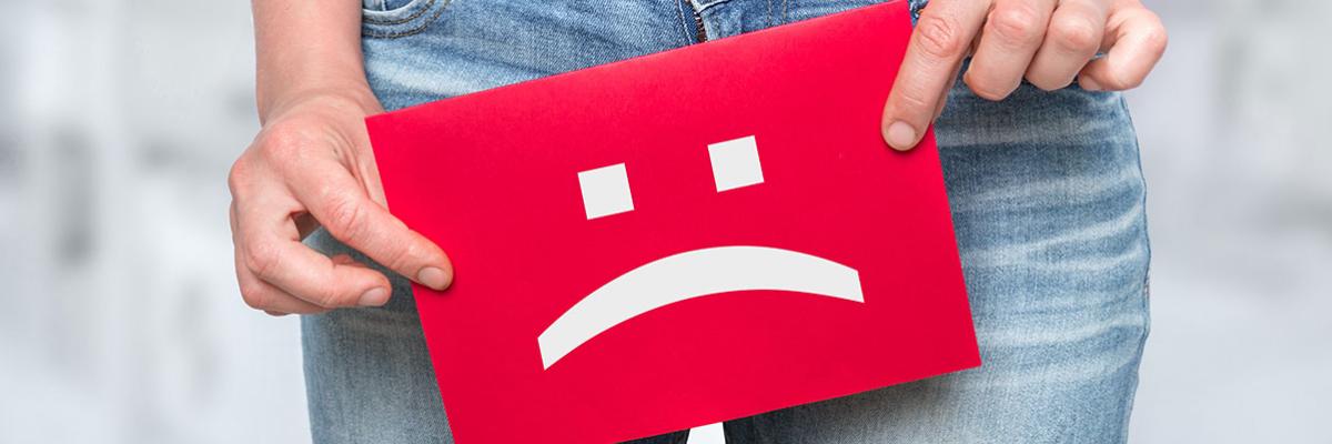 Jemand hält sich ein Schild mit einem traurigen Smiley vor den Schoß