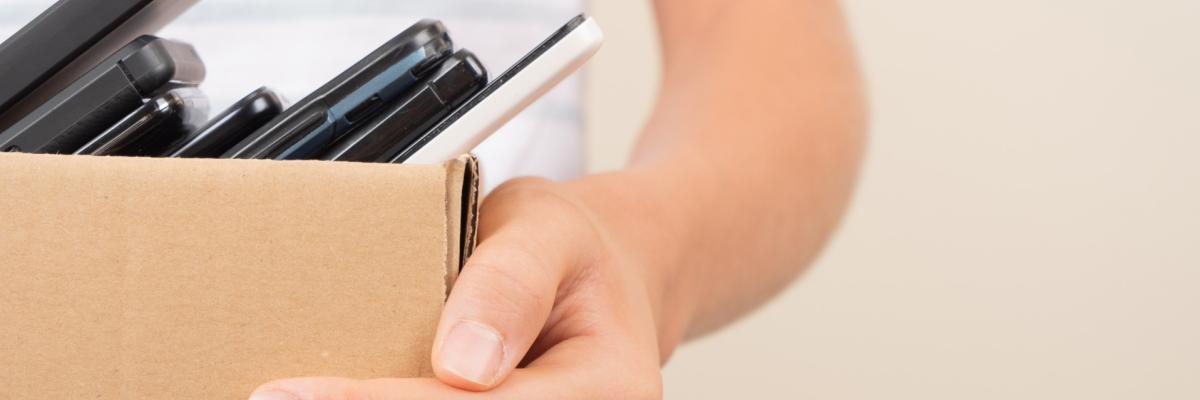     Anfrage erfolgreich  Hier ist ein passender Alt-Text für das Bild:  Nahaufnahme einer Person, die einen kleinen Pappkarton hält, der mit mehreren alten Mobiltelefonen und Smartphones gefüllt ist.