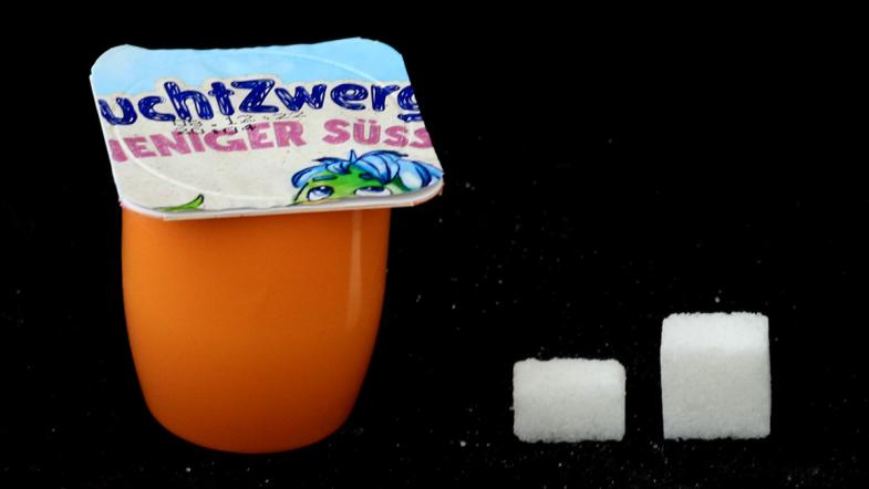 Joghurtbecher von Fruchtzwerge und daneben eine Zuckerwürfel-Pyramide