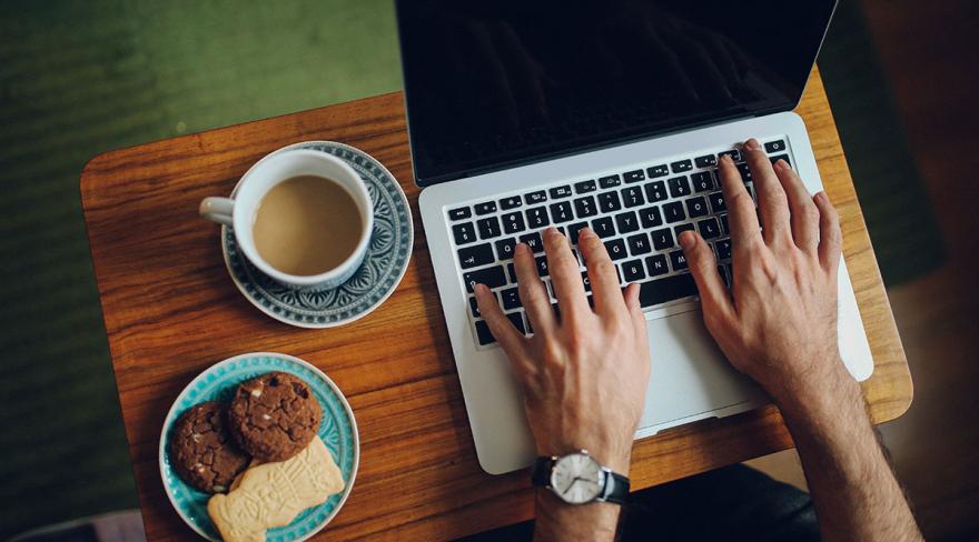 Cookies: Männerhände auf einem Laptop, daneben stehen ein Teller mit Keksen und eine Tasse