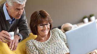 Paar mittleren Alters schaut zusammen in den Laptop auf der Couch.