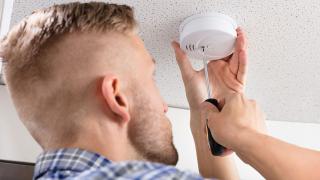 Ein junger Mann montiert einen Rauchmelder an der Decke