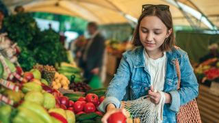 Eine Frau kauft Gemüse ein und packt es in eine Netztasche  