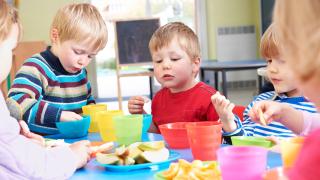 Mehrere Kinder sitzen am Tisch in der Kita und essen Obstschnitze 