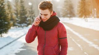 Ein Junger Mann trägt eine rote Fleecejacke. Er läuft auf einer winterlichen Straße und telefoniert.  