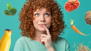 Eine junge Frau mit roten Locken blickt nachdenklich nach oben, um sie herum sind verschiedene gesunde Lebensmittel angeordnet 