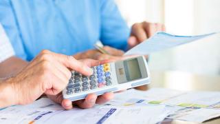 Hände zweier älterer Personen mit Unterlagen und einem Taschenrechner