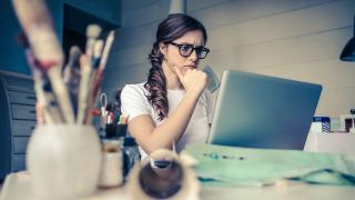 Eine Frau sitzt mit kritischem Blick am Schreibtisch vor ihrem Laptop