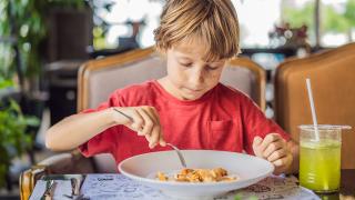Ein Kind in einem Restaurant isst auf einem Teller.