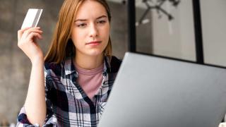 Eine Frau sitzt mit skeptischem Blick vor einem Laptop, sie hält eine Kreditkarte in der Hand